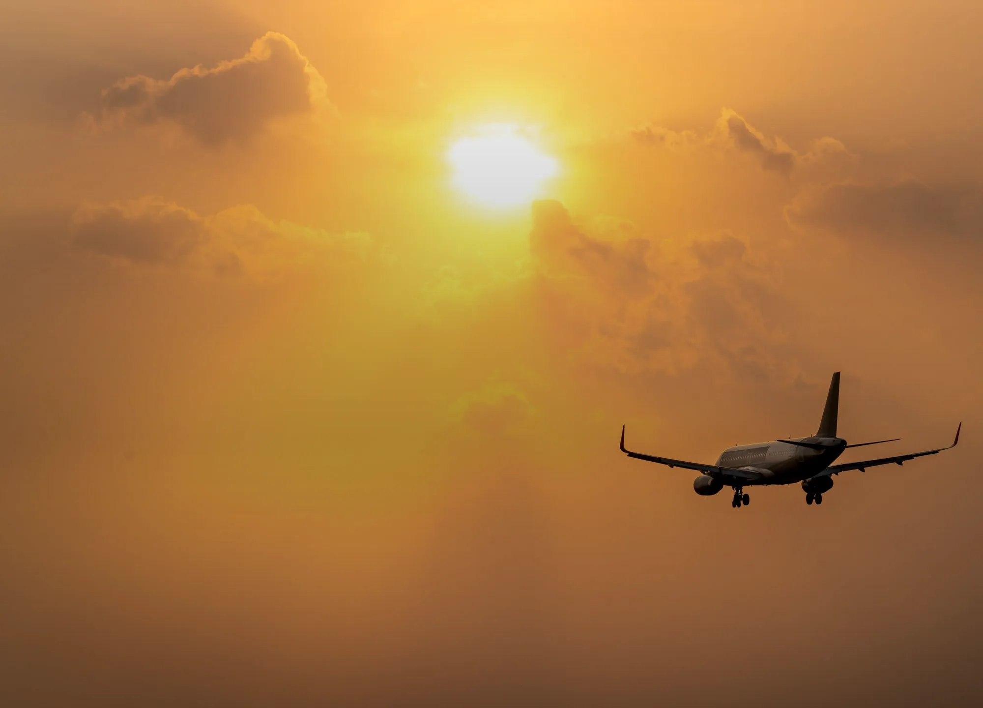 An airliner in silhouette against a sunset sky, its landing gear down